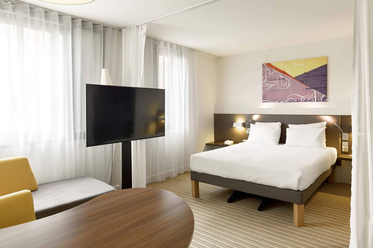 A hotel room with a bed, a TV, a desk, and a chair.