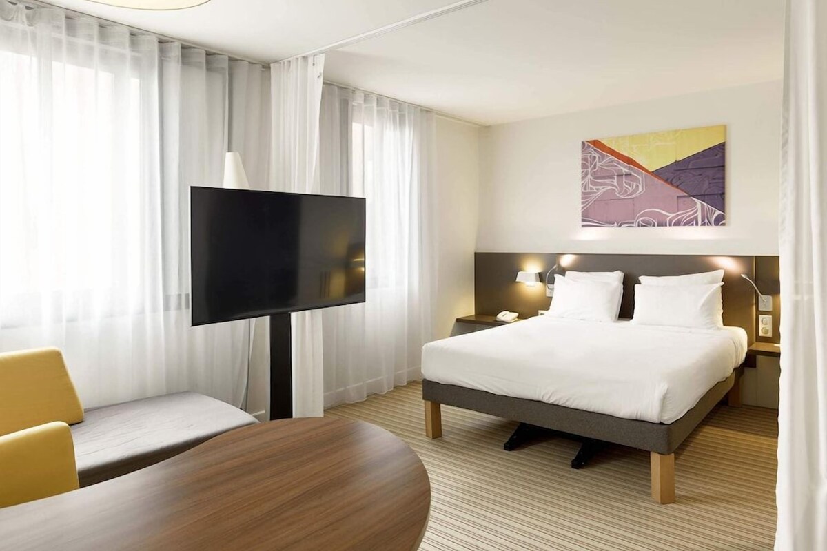 A hotel room with a bed, a TV, a desk, and a chair.