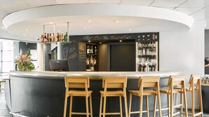 A modern bar area with a curved counter, wooden stools, and a variety of bottles and glasses. - B&B HOTEL Paris Grand Roissy CDG Aéroport (Roissy-en-France)
