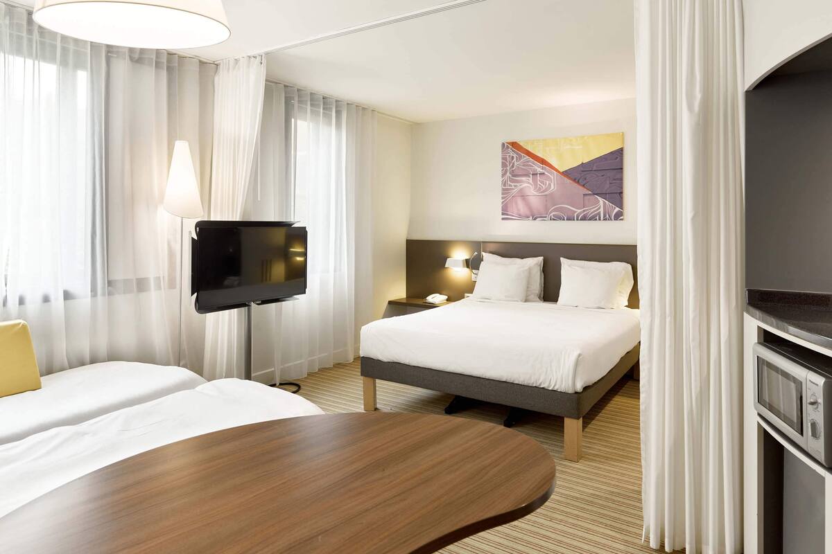 A hotel room with a bed, a TV, a bedside table, and a lamp.
