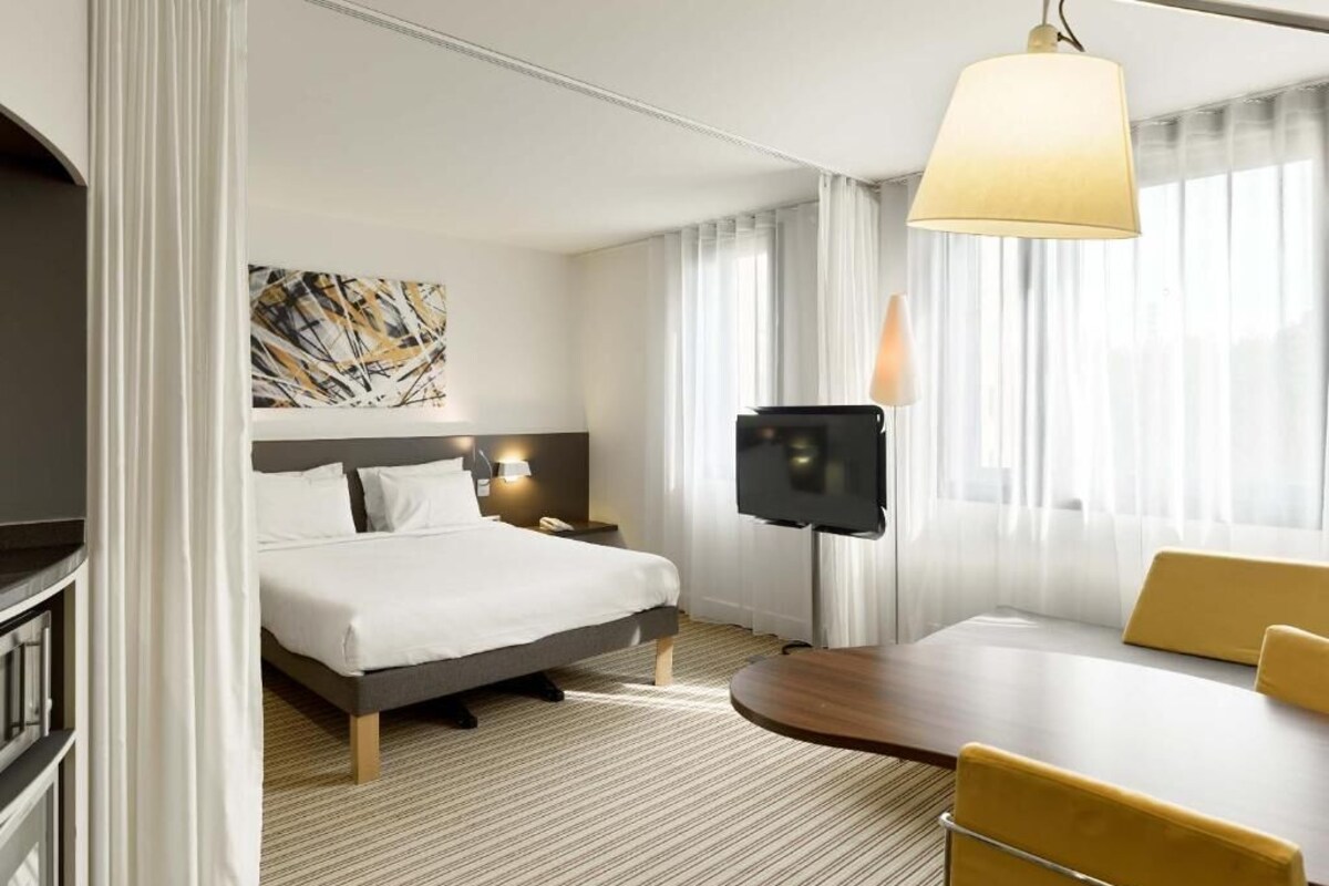 A hotel room with a bed, a desk, a TV, and a large window with curtains.