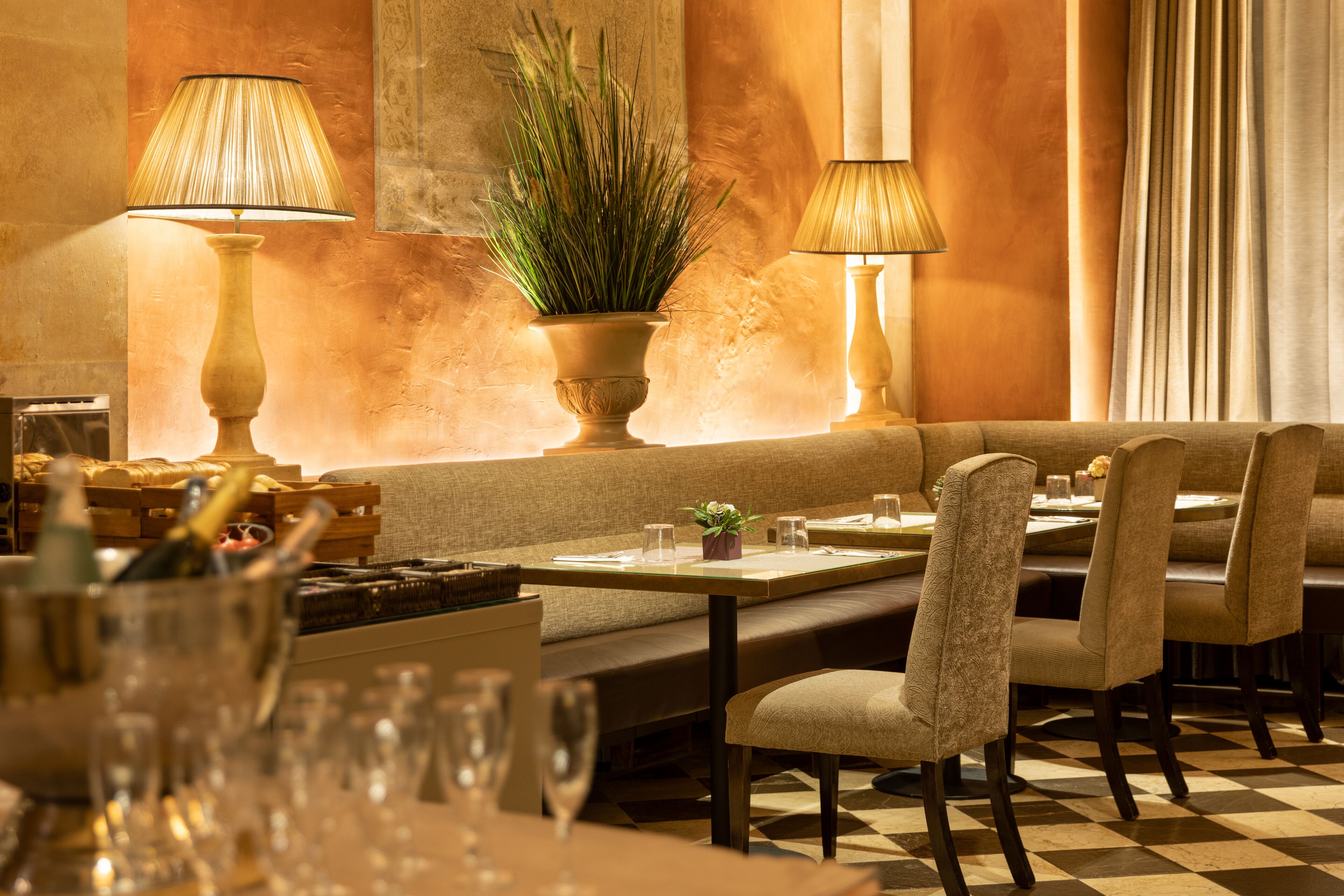 A restaurant with a checkered floor, cushioned seating, and two lamps.