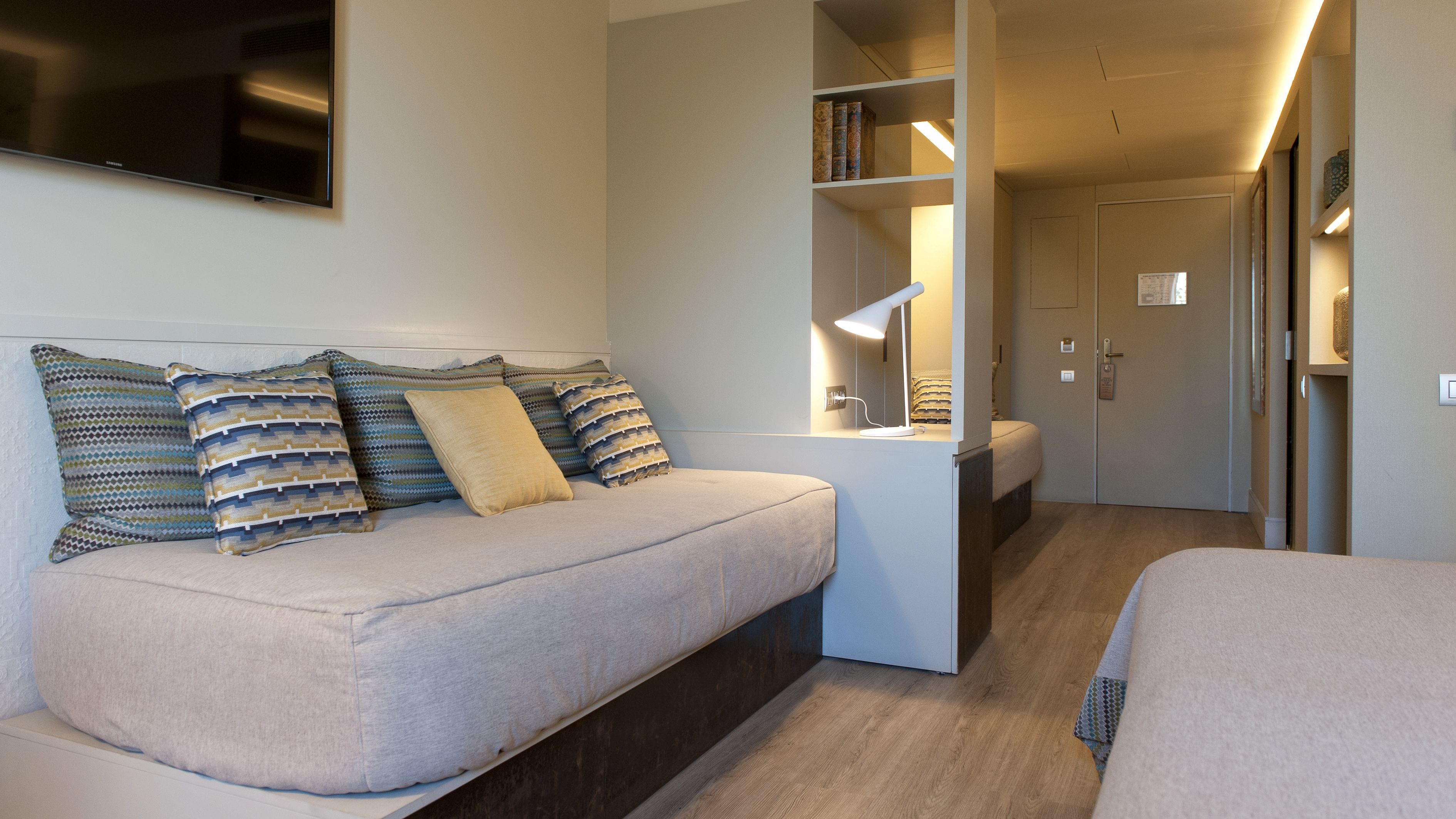 A modern, well-lit bedroom with a sofa, a bedside table with a lamp, and a wardrobe.