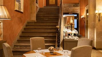 Un espace repas comprenant une table ronde, quatre chaises, un lustre, un escalier et des œuvres d’art encadrées accrochées aux murs.
