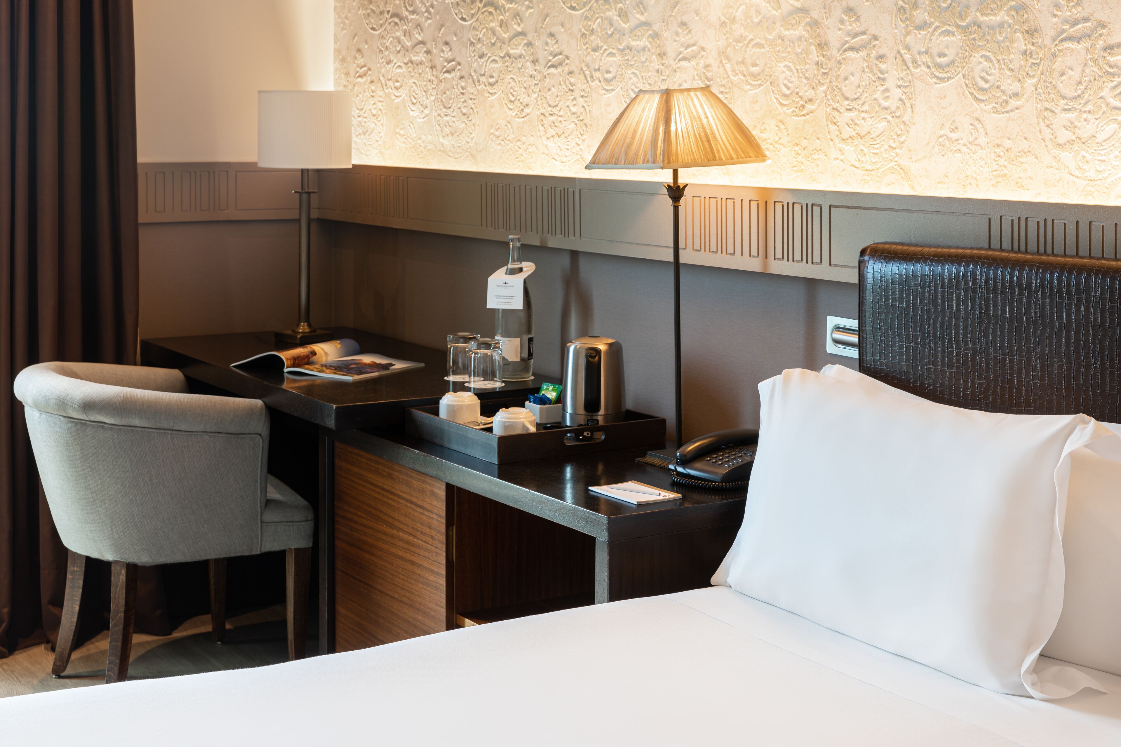 A hotel room with a desk, chair, bed, lamp, and a telephone.