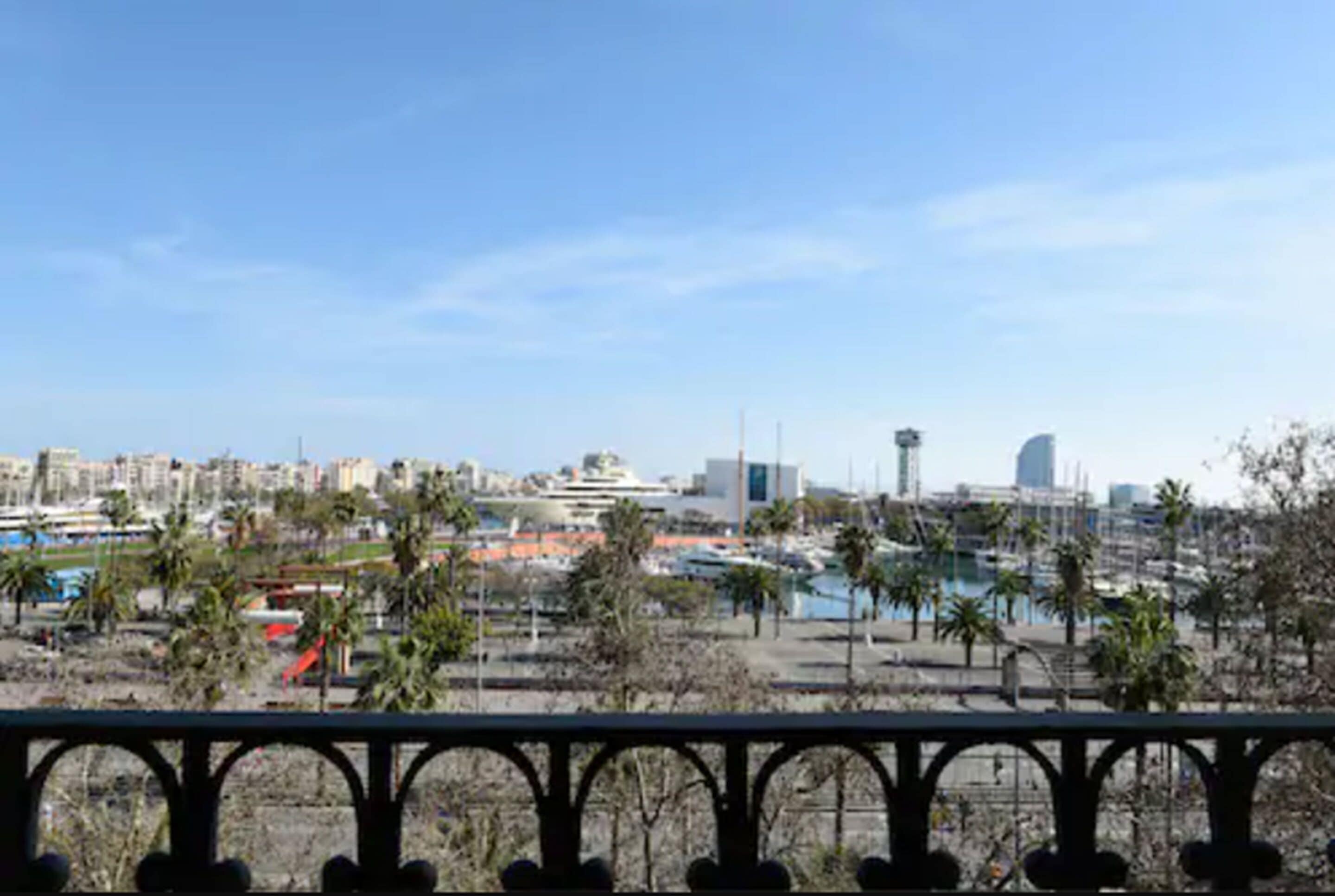 A coastal cityscape with modern buildings, a marina, and palm trees.