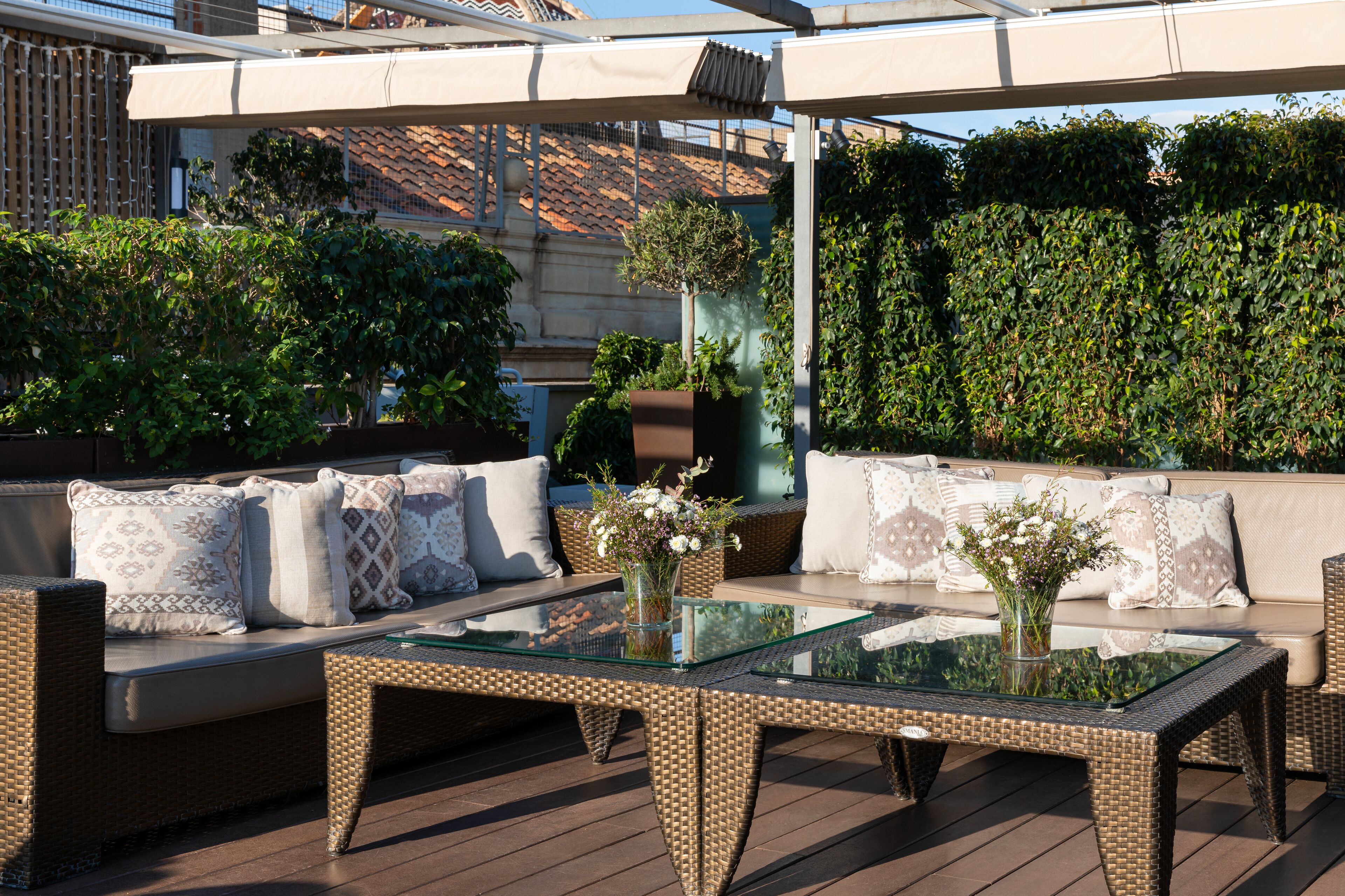Un espace extérieur aménagé avec des meubles en osier, des tables à plateaux de verre et une variété de plantes.