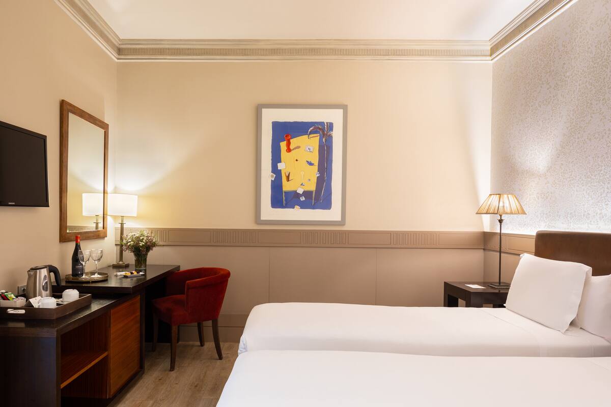 Ein Hotelzimmer mit einem Bett, einem Schreibtisch mit Stuhl, einem Fernseher und einem gerahmten Kunstwerk an der Wand.