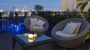 Um terraço com cadeiras de vime, uma mesa de vidro, um vaso de planta e velas.