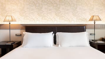 A neatly made bed with two white pillows, a dark headboard, and two bedside tables with lamps and a book on each.