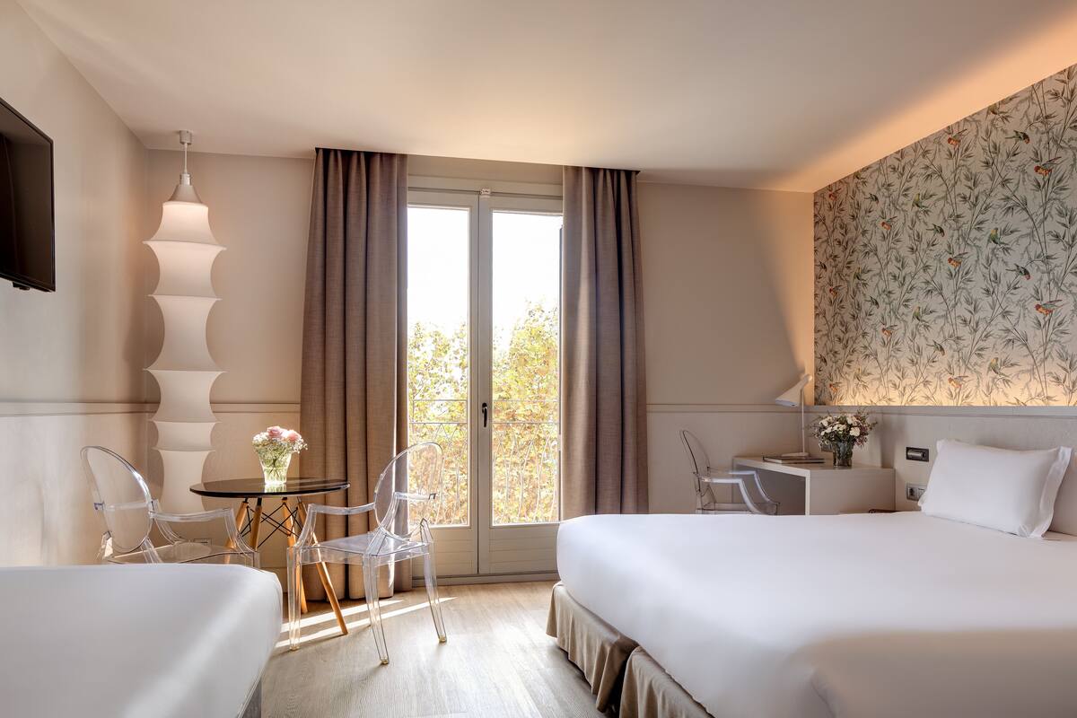 Ein Hotelzimmer mit zwei Betten, einem Schreibtisch, einem Stuhl, einem Fernseher und einem Vorhangfenster.