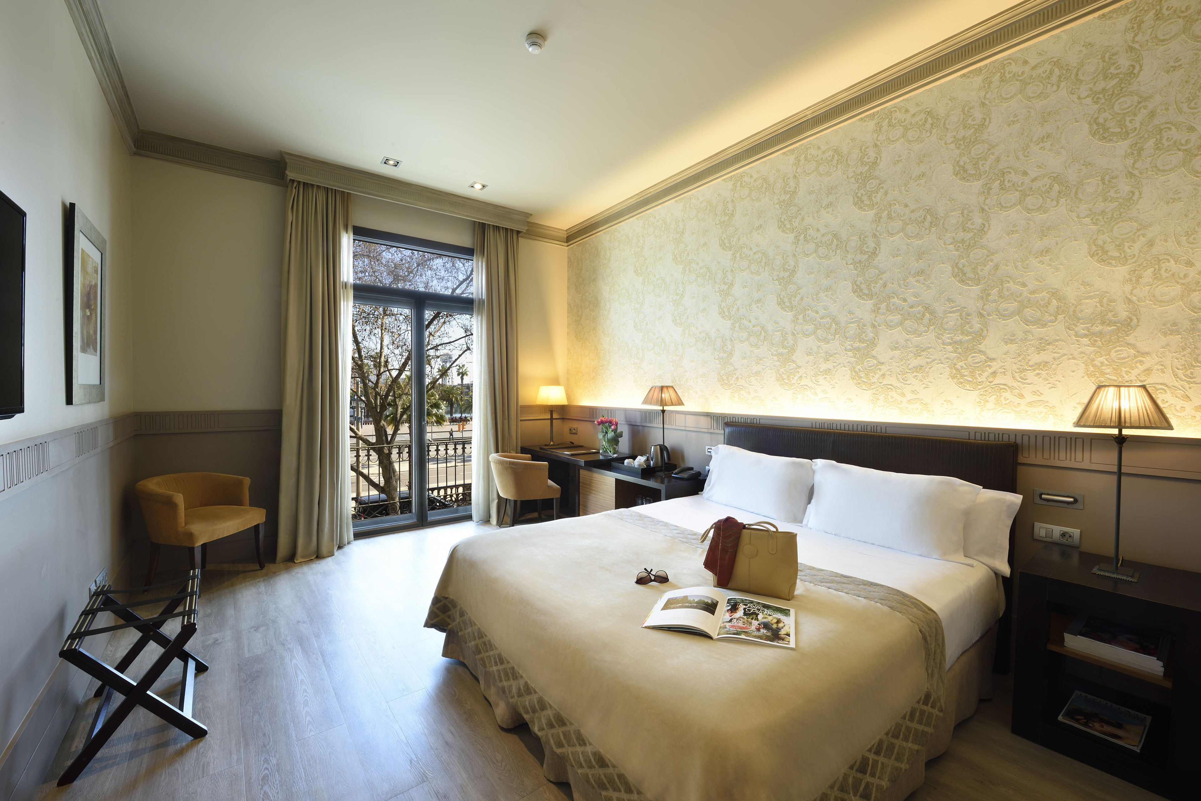 A hotel room with a large bed, a desk, a chair, and a view of the outdoors.