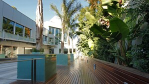 A wooden deck with benches, surrounded by lush greenery and a modern building with large windows.