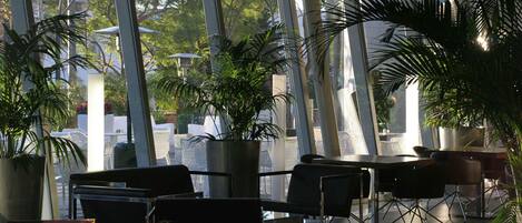 A modern indoor space with large windows, potted plants, and contemporary furniture.