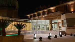 An outdoor area with a modern building entrance, a covered seating area, and decorative lighting.