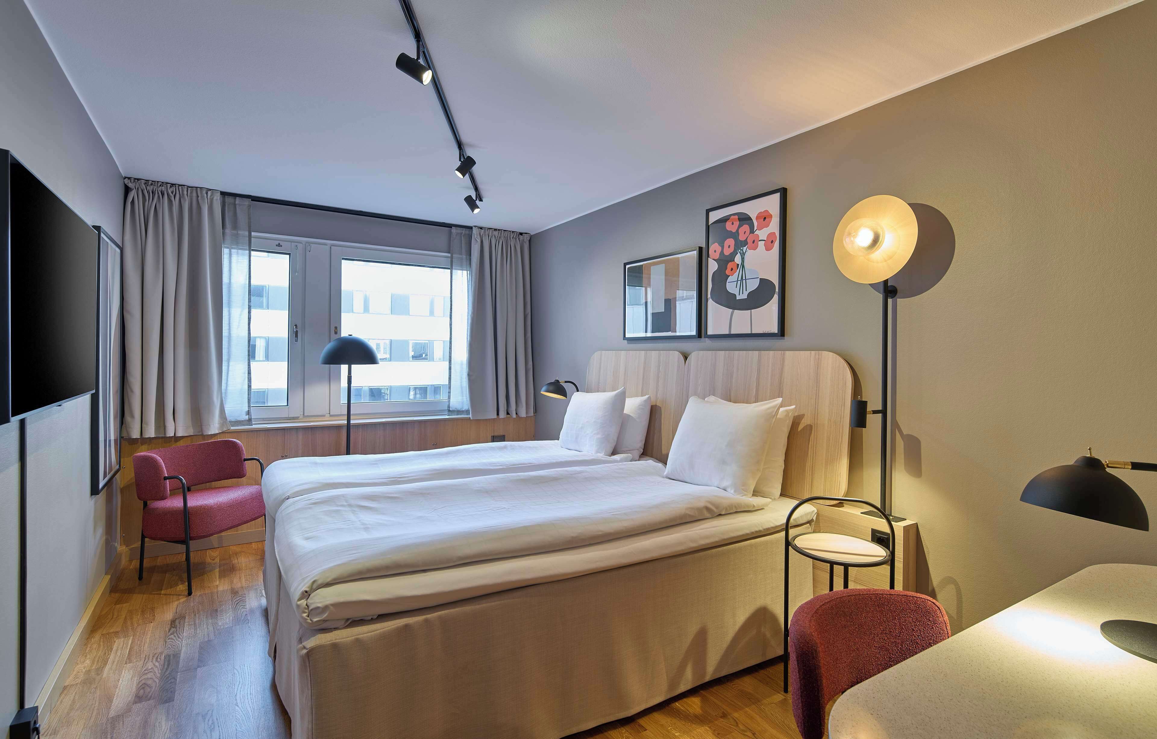 Habitación de hotel con una cama grande, un escritorio, una silla, un televisor y una ventana con cortinas.