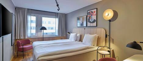 A hotel room with a large bed, a desk, a chair, a TV, and a window with curtains.