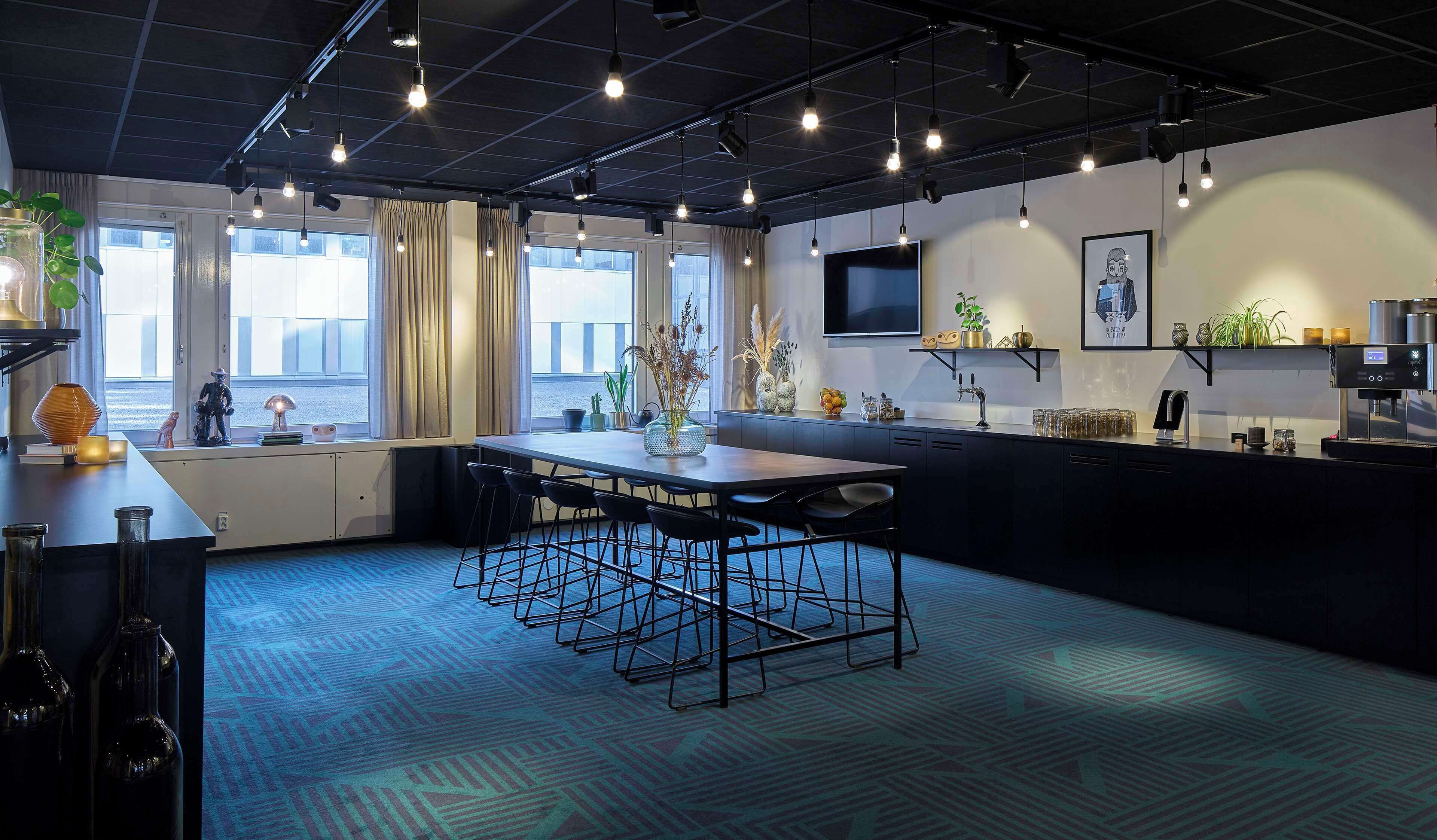 A modern kitchen with a central island, bar stools, a coffee machine, and a TV mounted on the wall.
