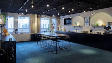 A modern kitchen with a central island, bar stools, a coffee machine, and a TV mounted on the wall.
