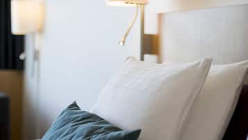 Una cama bien hecha con almohadas, una lámpara de pared y cuadros en la pared.