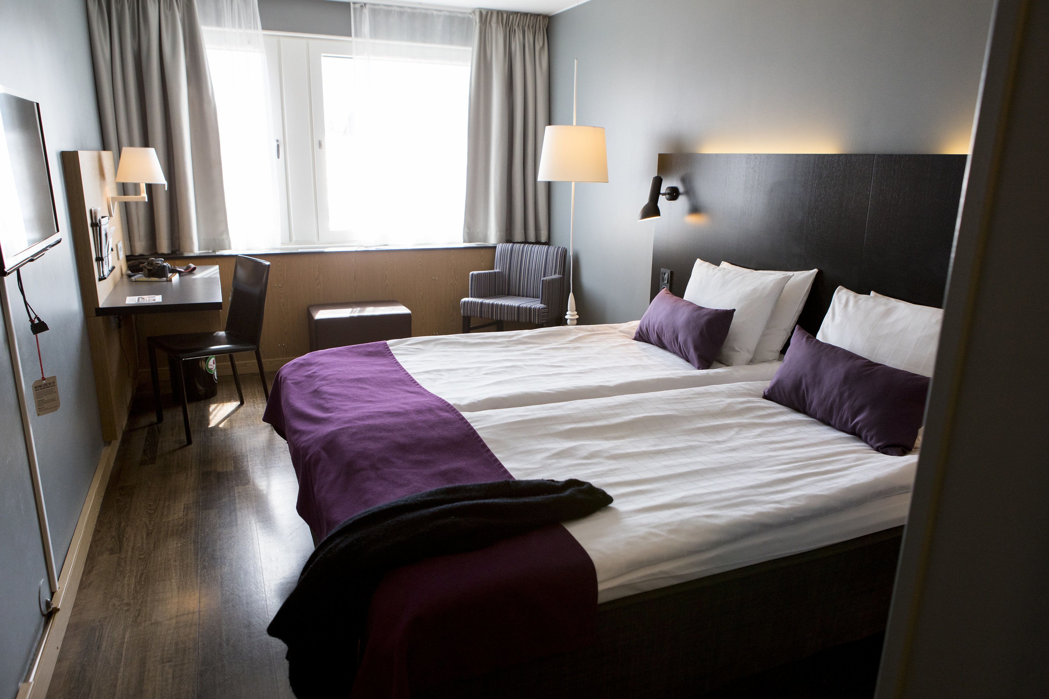 A hotel room with two beds, a desk, a chair, and a TV.