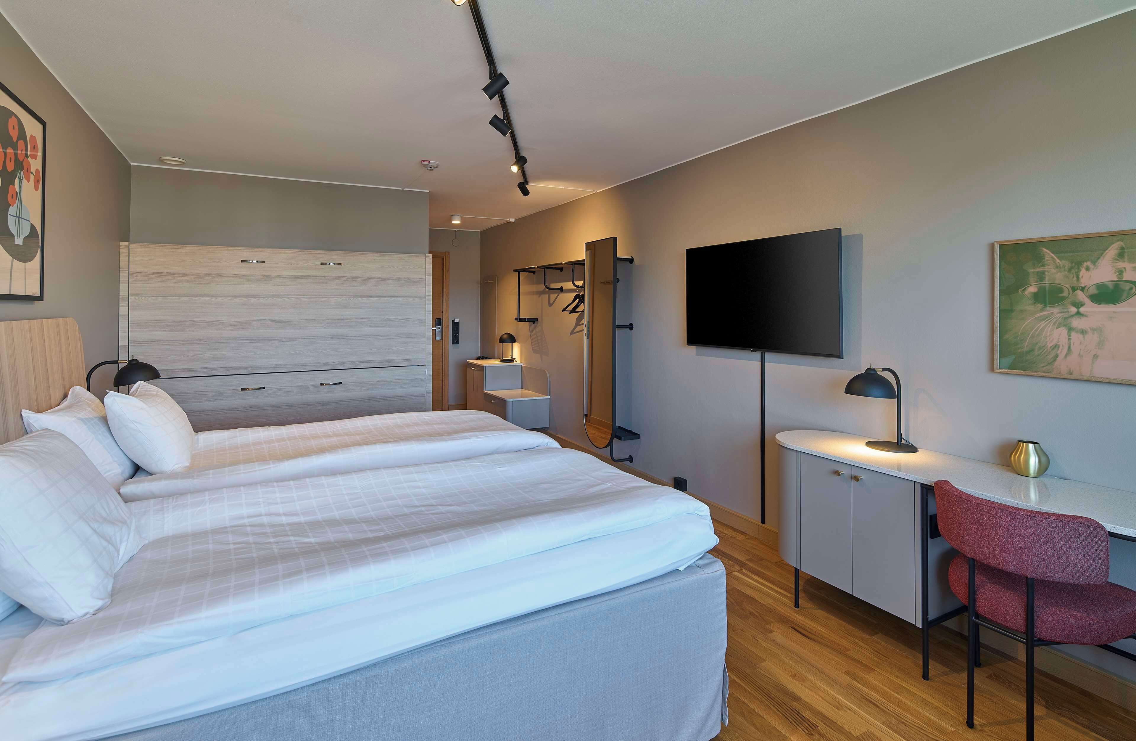 Ein modernes Hotelzimmer mit einem großen Bett, einem Schreibtisch mit Stuhl, einem Flachbildfernseher und einem Spiegel.