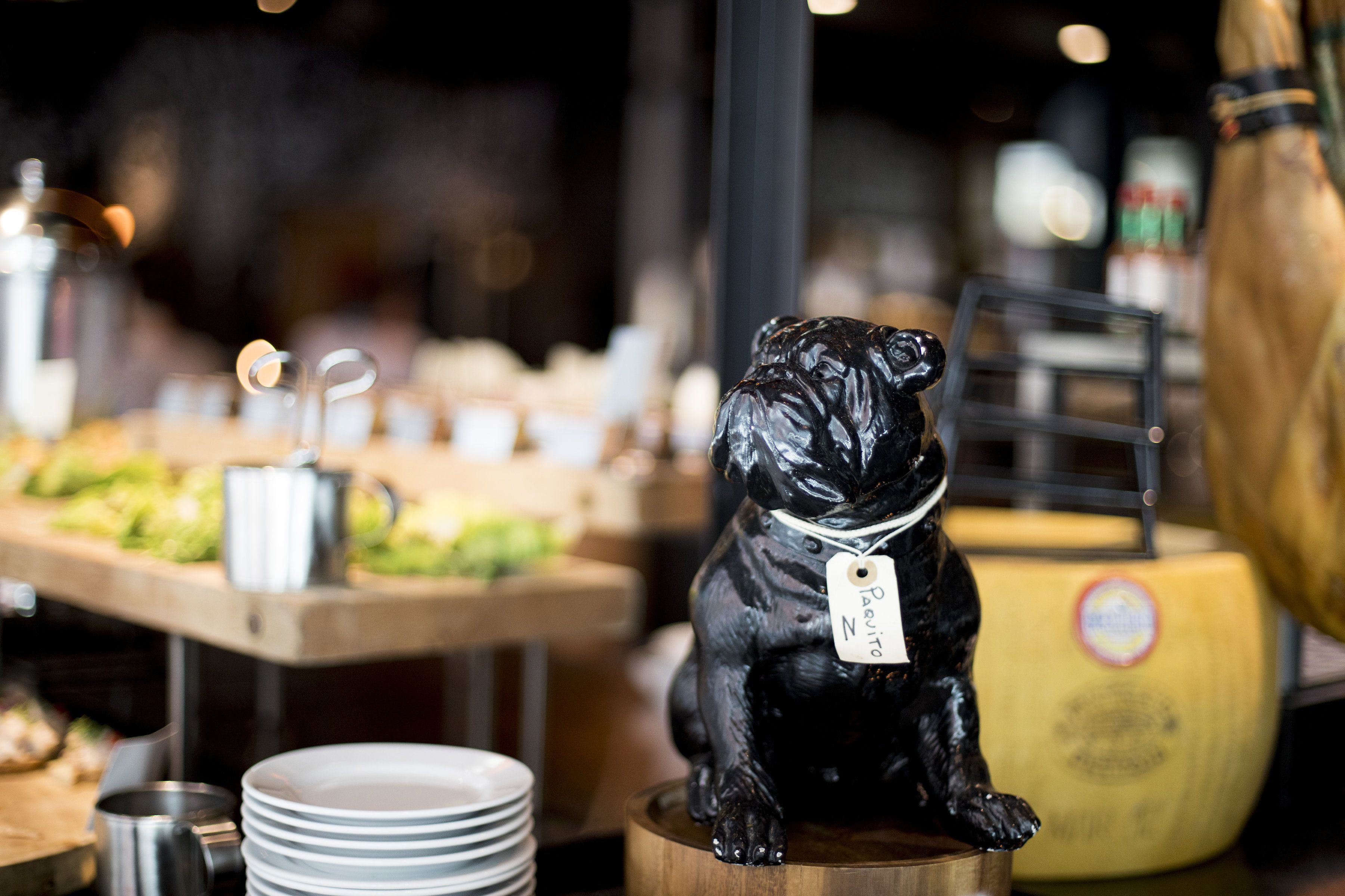 A black dog figurine on a wooden stand with a tag, surrounded by plates and a yellow container.