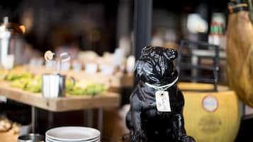 A black dog figurine on a wooden stand with a tag, surrounded by plates and a yellow container.