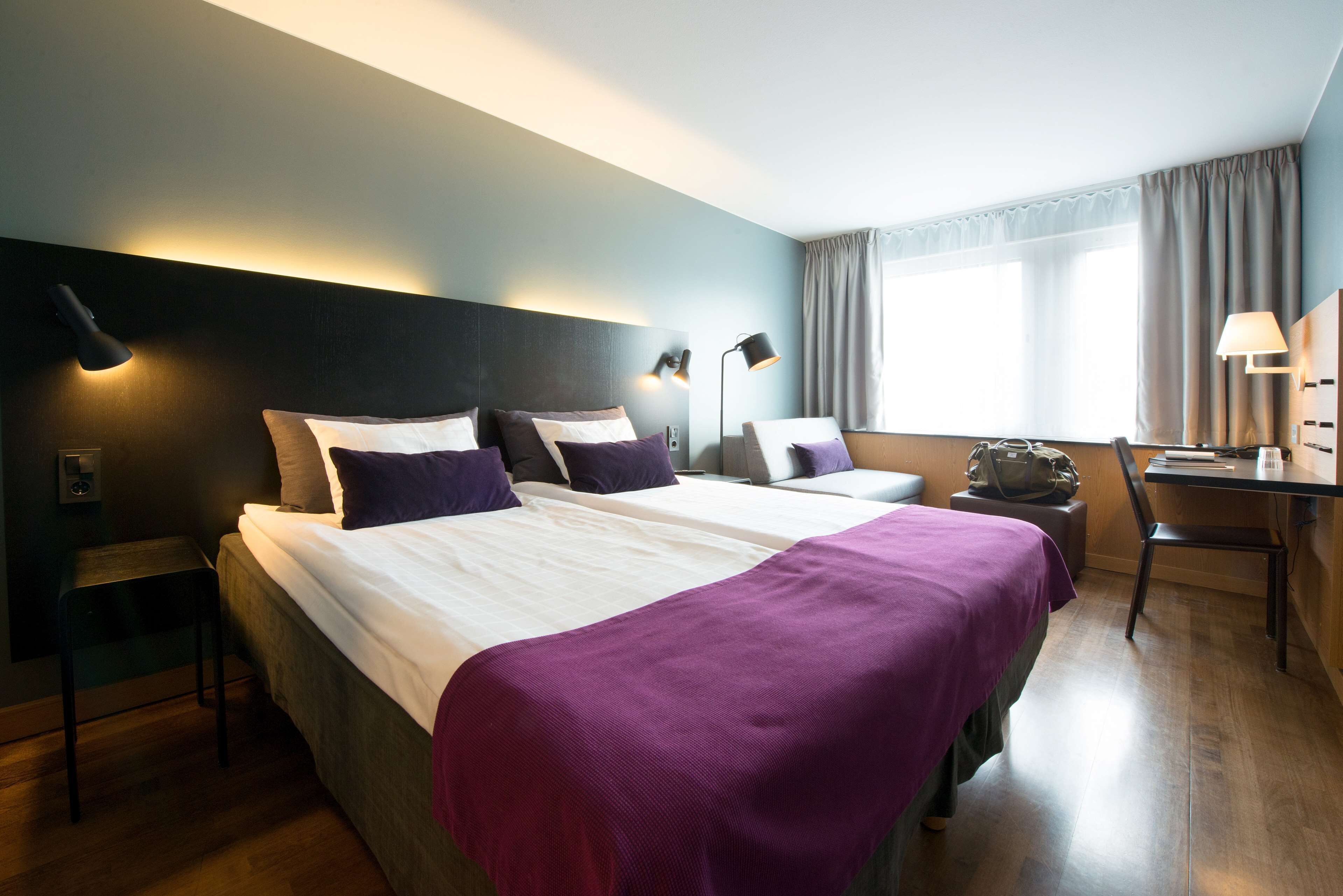 A hotel room with two beds, a desk, and a chair.