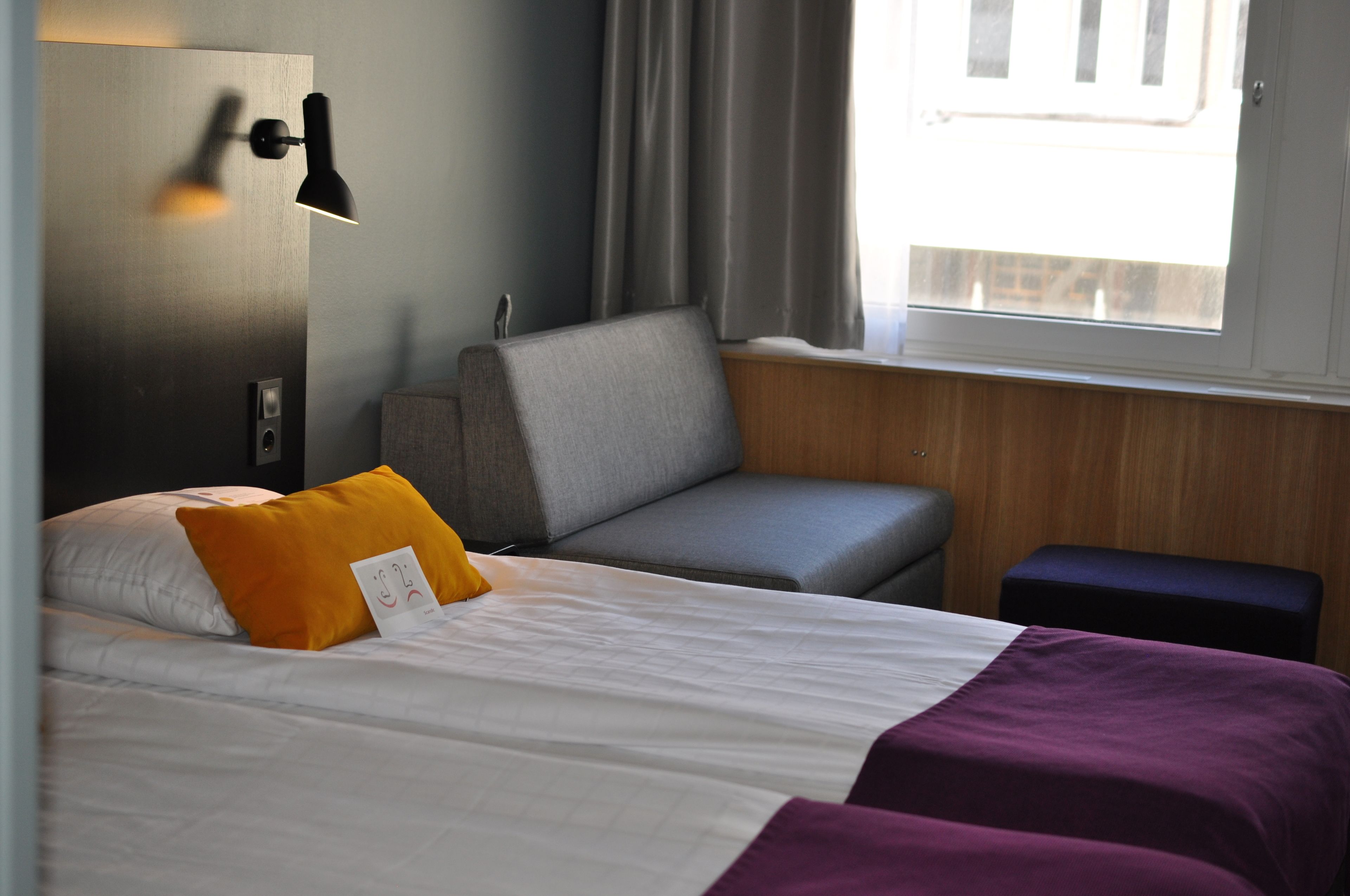 Ett hotellrum med en säng, en soffa, ett litet bord och ett fönster med gardiner.