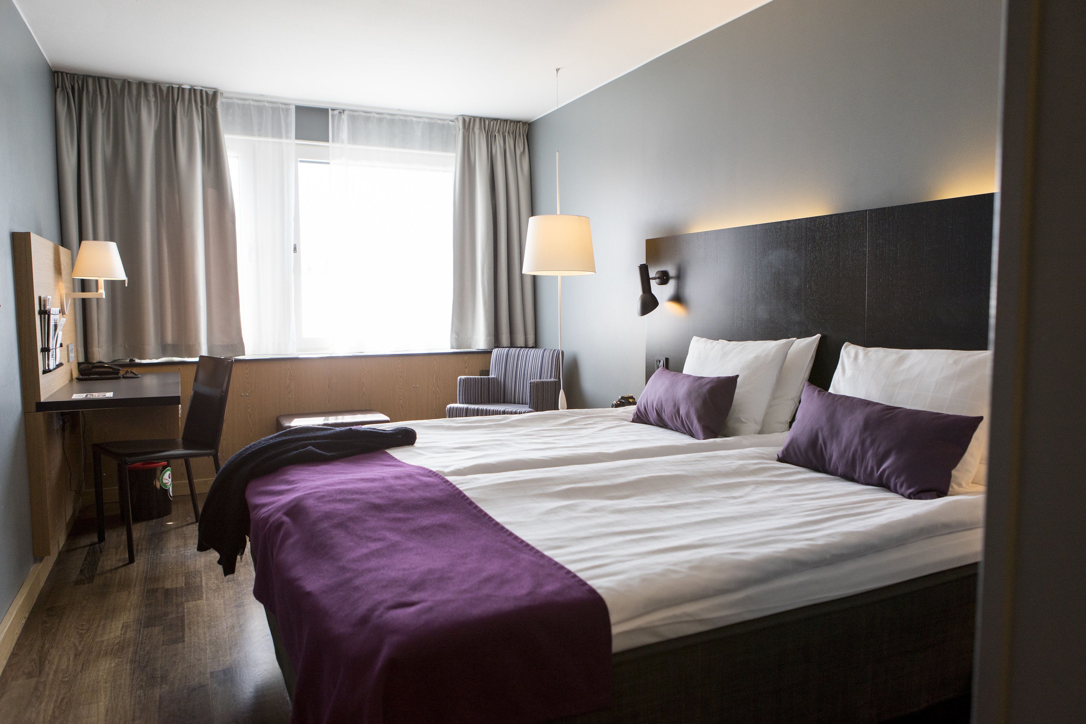 Habitación de hotel con dos camas, un escritorio, una silla y una ventana con cortinas.