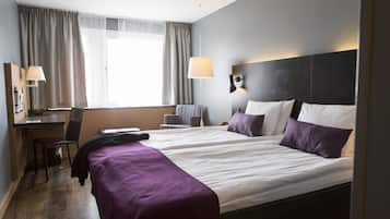 Habitación de hotel con dos camas, un escritorio, una silla y una ventana con cortinas.