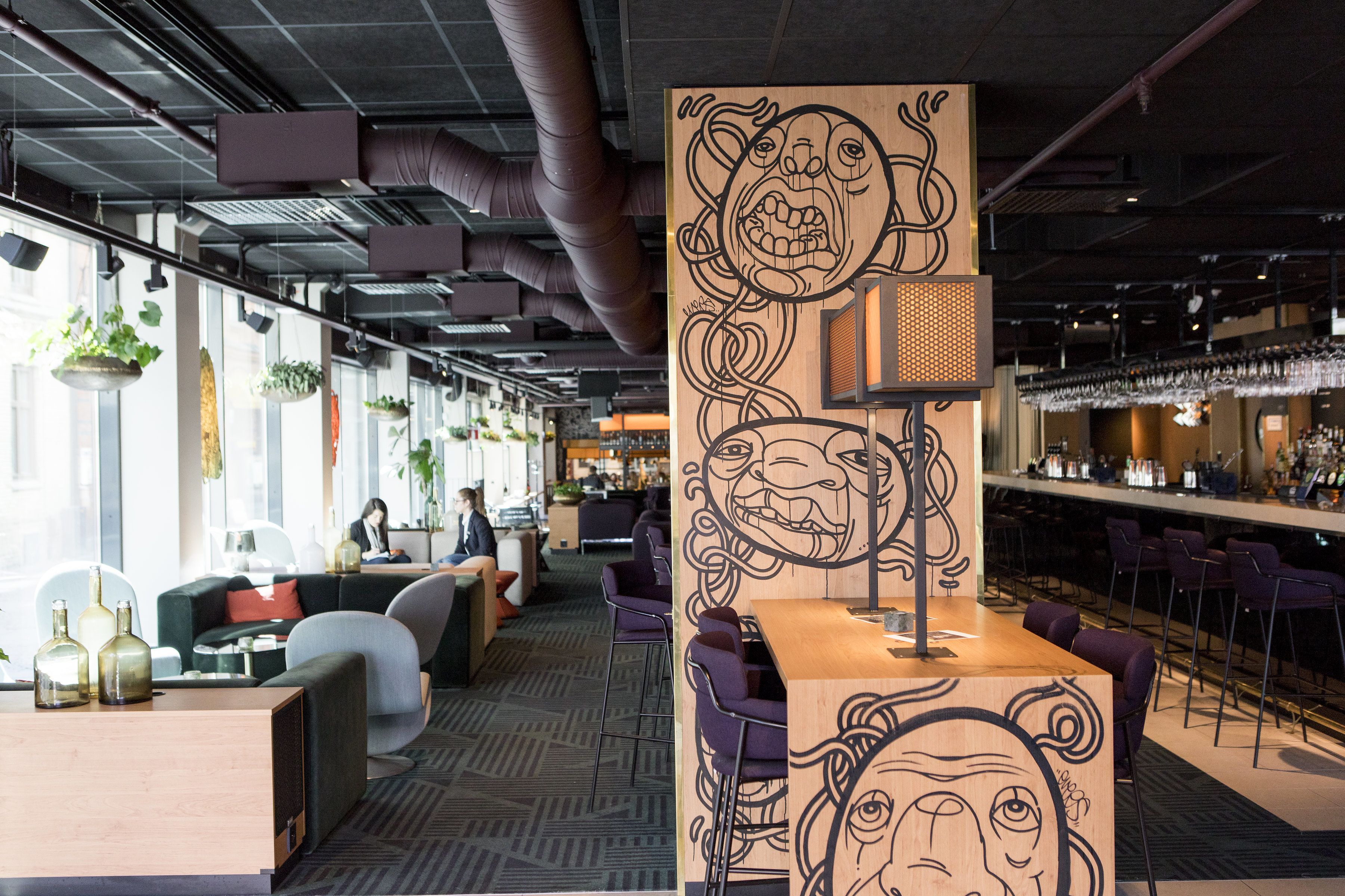 Zona de bar moderna con taburetes morados, una pared de madera con diseño facial y un área de estar con sofás y sillones.