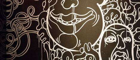 Un comedor con una mesa dispuesta para dos personas, una pared decorativa con diseños abstractos y dos lámparas colgantes.