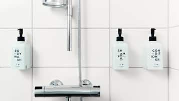Ein Badezimmer mit Duschkopf, Handbrause und drei Flaschen mit Badesiegel, Shampoo und Conditioner an der Wand.
