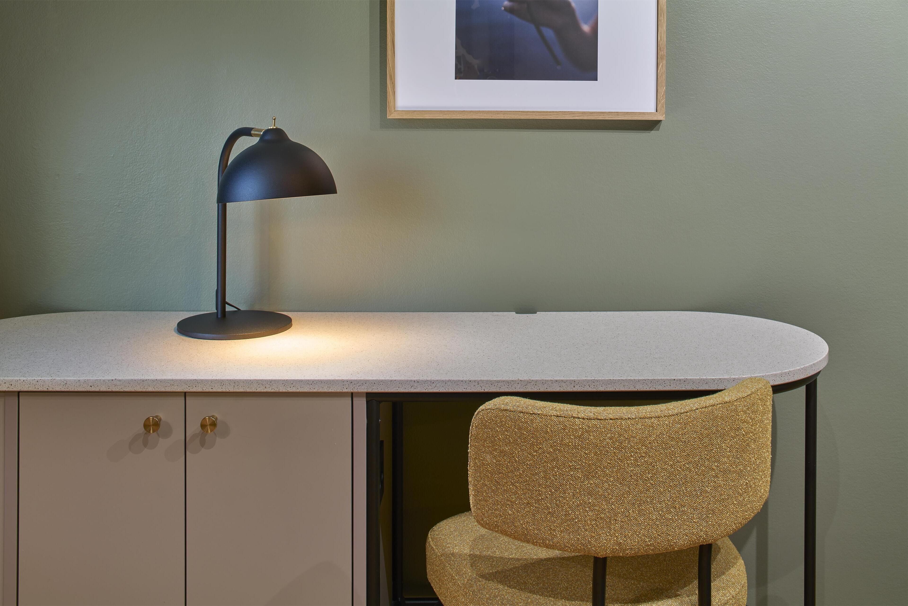 A desk with a lamp, a chair, and a framed picture on the wall.