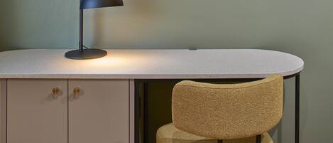 A desk with a lamp, a chair, and a framed picture on the wall.