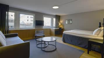 A hotel room with a bed, a desk, a chair, a small table, and a TV.