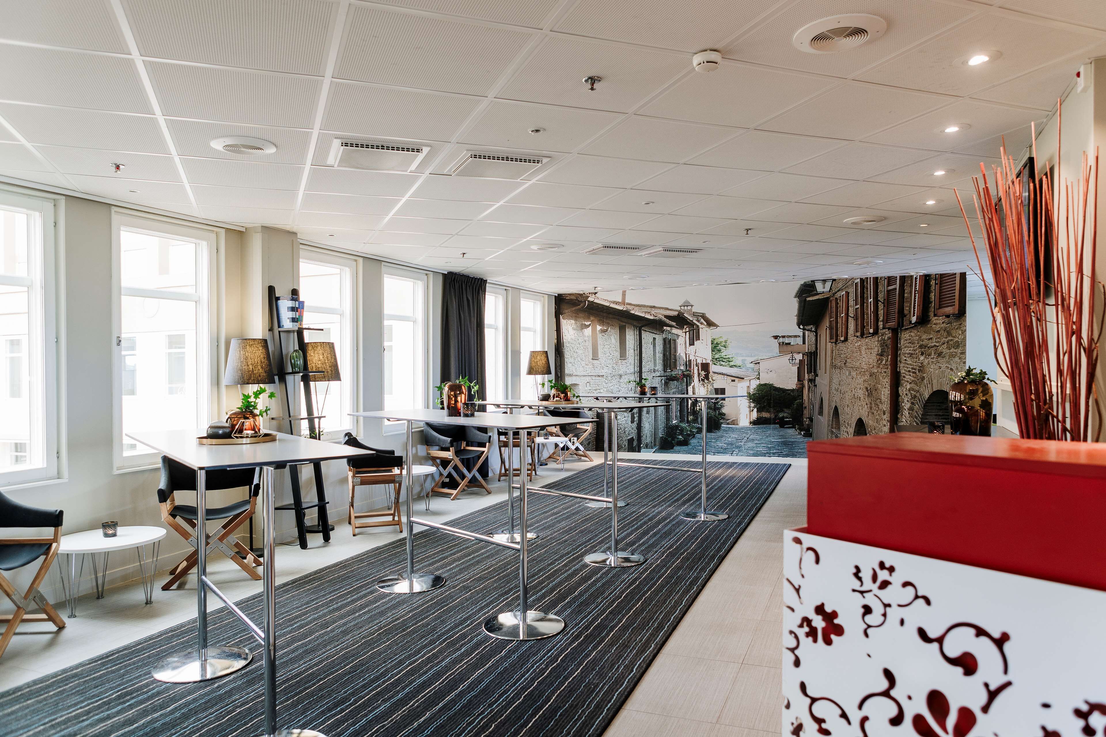 A modern hotel lobby with a long reception desk, multiple seating areas, and large windows offering views of the street.