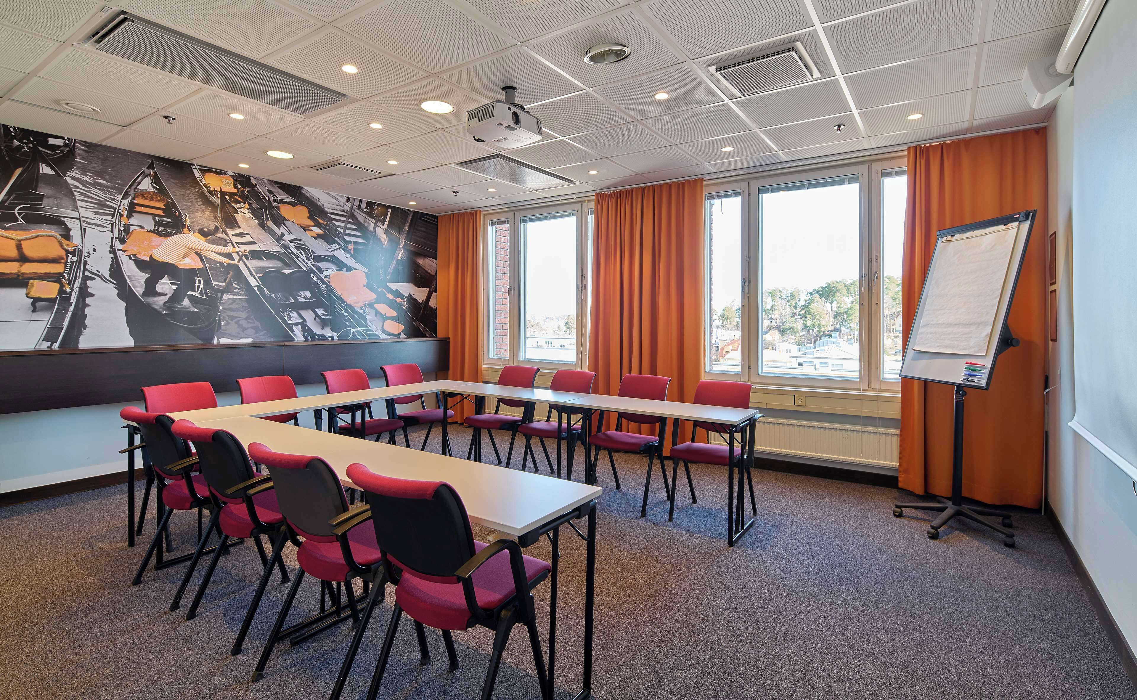 A conference room with a long table, red chairs, a whiteboard, and a mural on the wall.