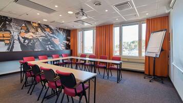A conference room with a long table, red chairs, a whiteboard, and a mural on the wall.