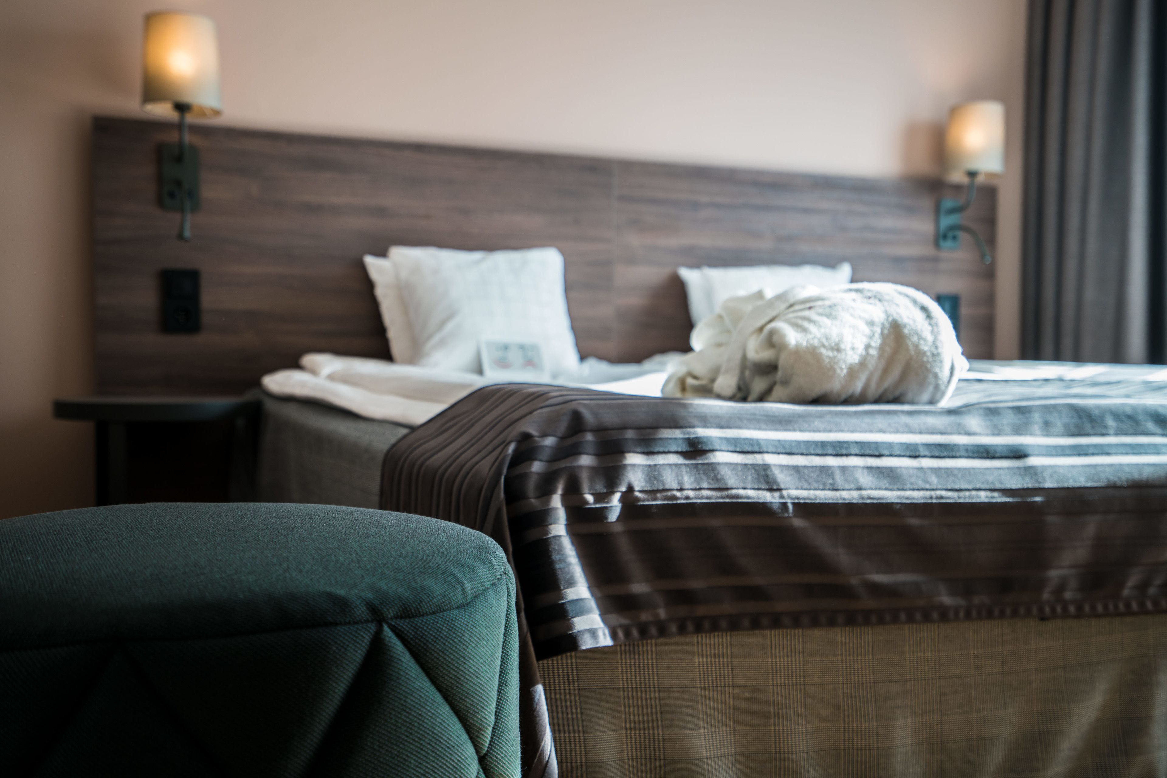 Una cama bien hecha con un edredón a rayas, una almohada y un cabecero con luces fijadas a la pared.