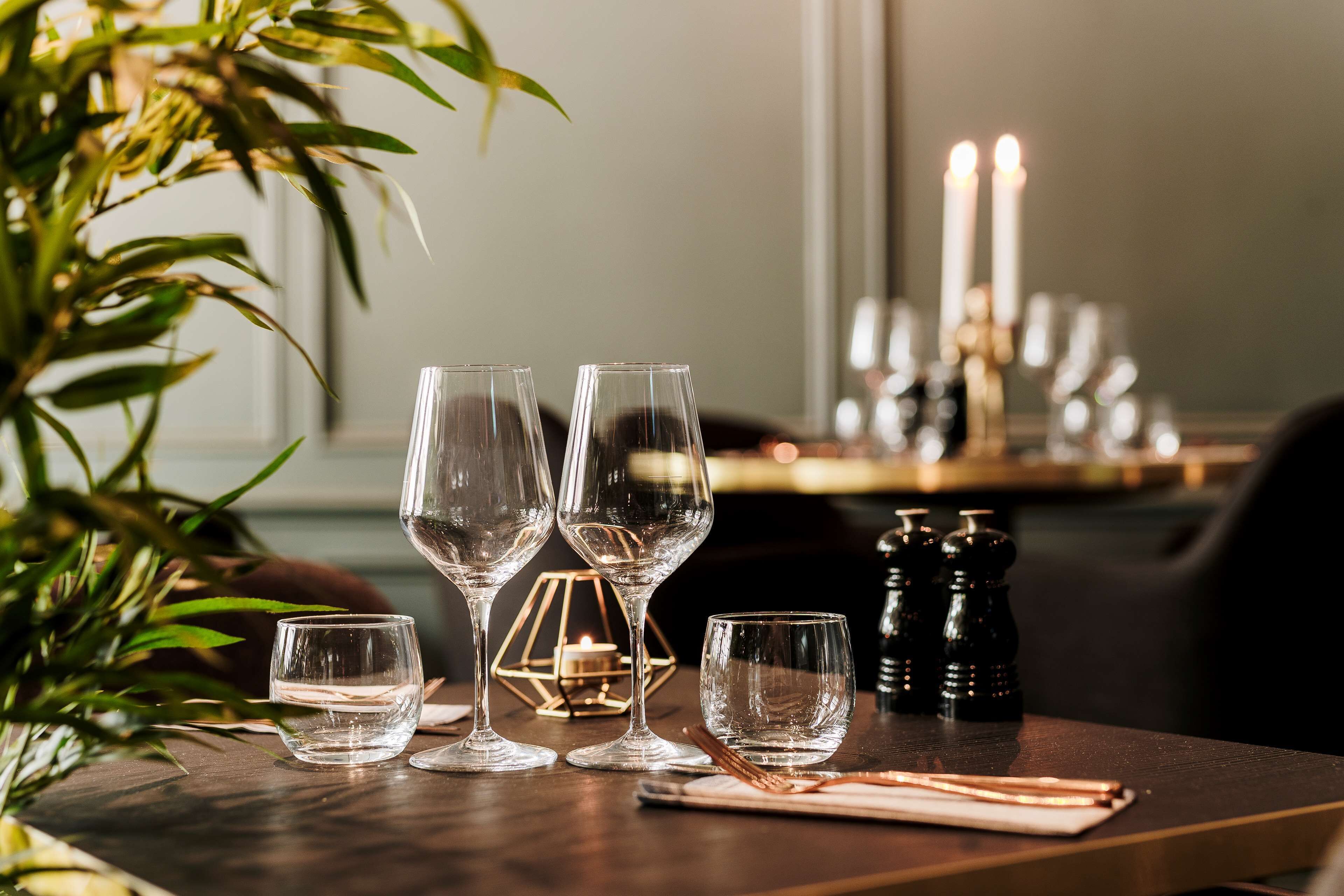 A dining table with four wine glasses, a candle, salt and pepper shakers, and a candle holder.