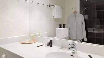 Un baño moderno con un espejo grande, azulejos blancos, un lavamanos y una zona de ducha.