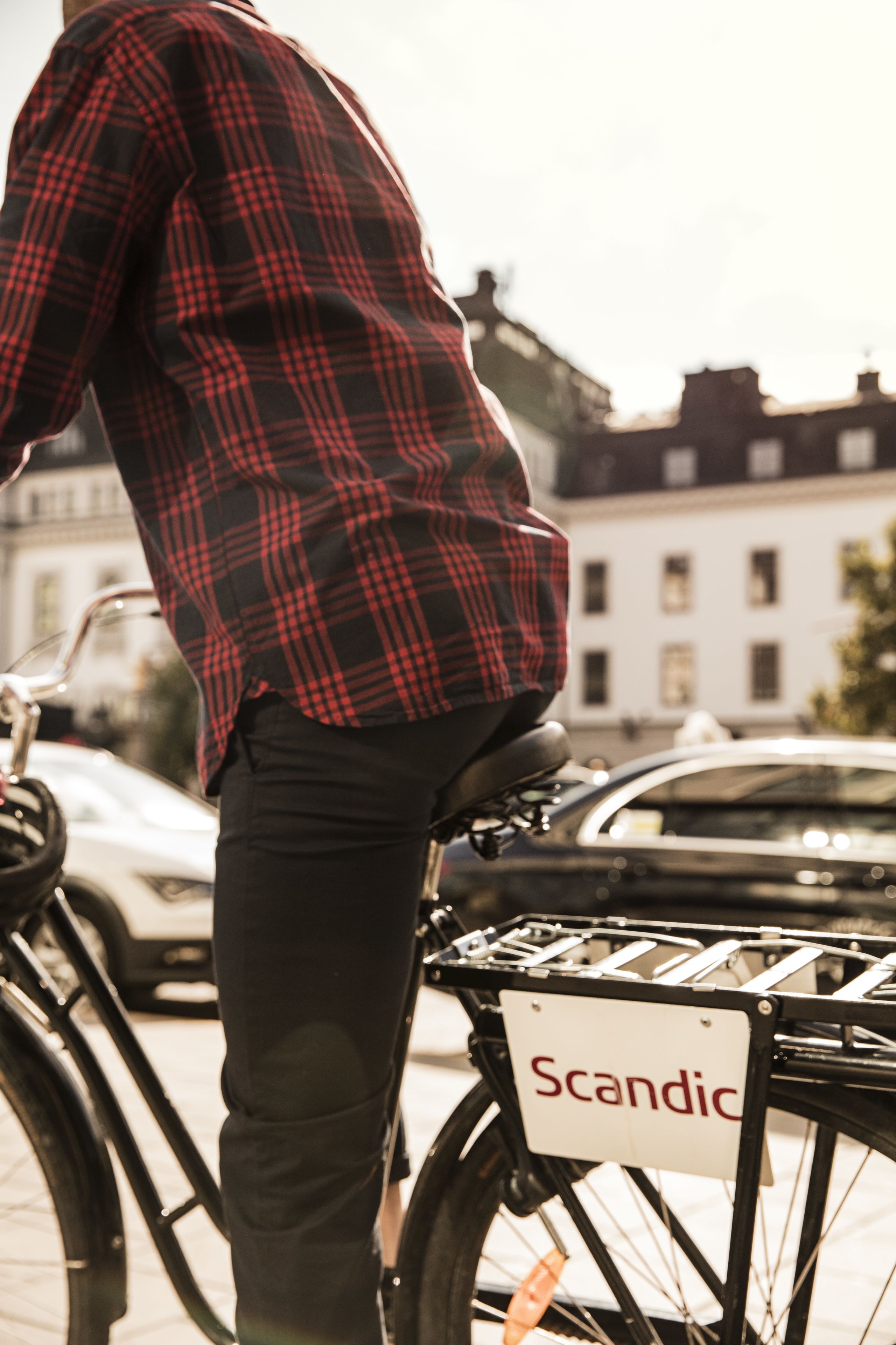 A person standing next to a bicycle with a basket labeled "Scandic".