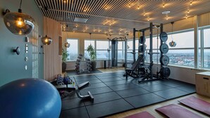 Un gimnasio con equipamiento de ejercicio, una pelota de ejercicios grande y vistas de la ciudad a través de amplias ventanas.