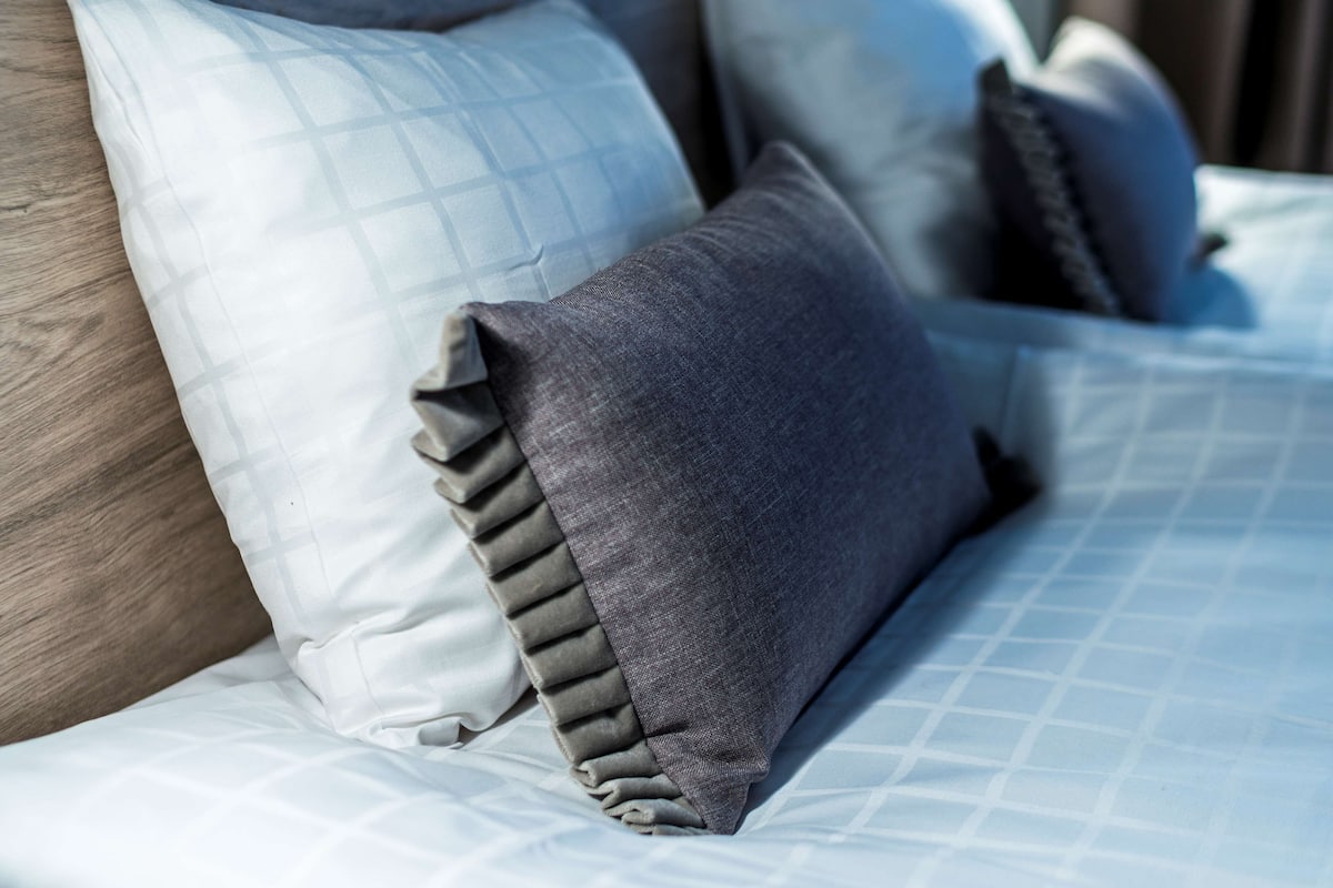 A bed with a patterned bedspread and multiple pillows, including a grey one with a ruffled edge.