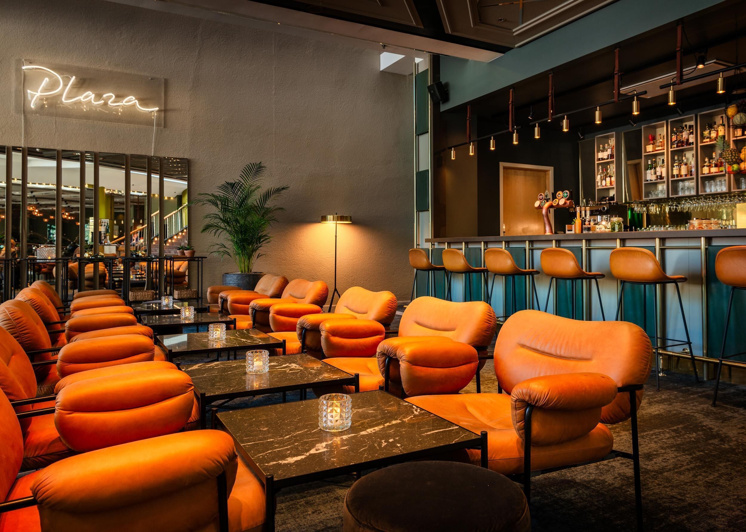 En bardel med orange läderstolar, en neonreklamskylt med texten ”Plaza” och en bar som är välfylld med flaskor.