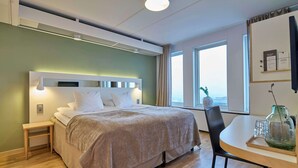 Una habitación de hotel moderna con cama, mesita de noche y un área de comedor con mesa y sillas.