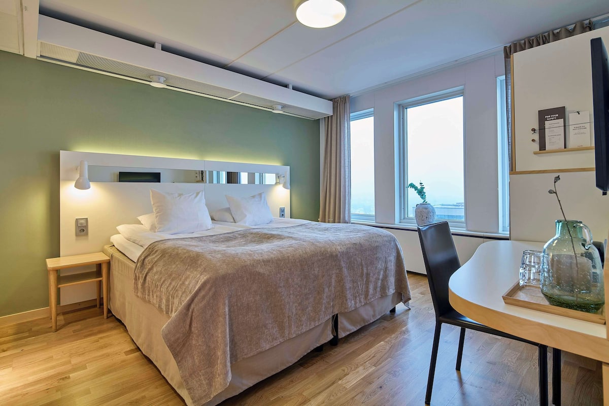 A modern hotel room with a bed, bedside table, and a dining area with a table and chairs.